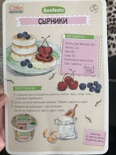 a person holding up a recipe book with pictures of cakes and berries on it's cover