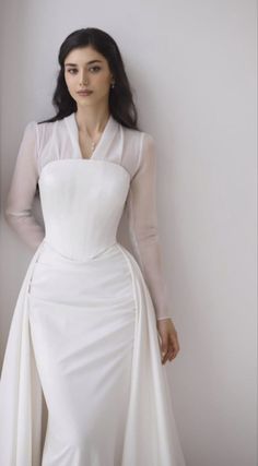 a woman in a white dress leaning against a wall with her hands on her hips