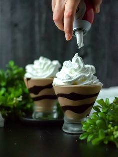 someone is adding whipped cream to some desserts in small cups on a table with greenery