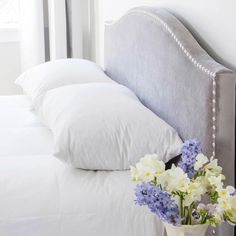 a vase with flowers sitting on top of a bed next to pillows and pillow cases