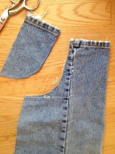 a pair of scissors next to an old pair of jeans cut in half on a wooden surface