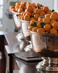 several silver bowls filled with oranges on top of a wooden table