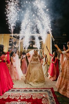 the bride and groom are surrounded by their guests as fireworks go off in the background