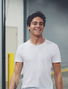 a man in white shirt and blue shorts holding a skateboard smiling at the camera