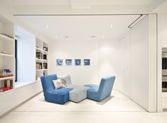 a living room with white walls and blue chairs in the center, along with shelves filled with books