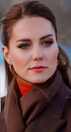 a woman with brown hair and blue eyes is wearing an orange shirt, black jacket and earrings