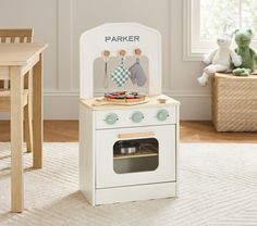 a white wooden toy oven sitting on top of a rug next to a table and chair