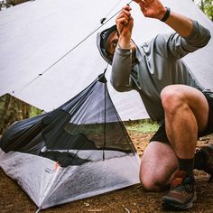 a man sitting on the ground next to a tent with his hands in the air