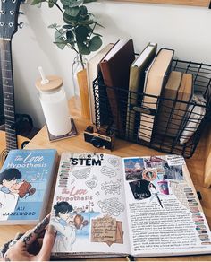 a person is holding a pen and looking at an open book on a table next to some books