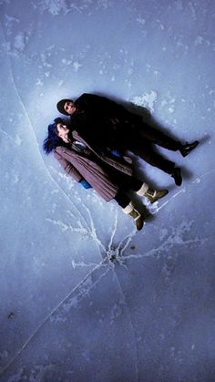 two people laying in the snow with their arms around each other and one person holding an umbrella