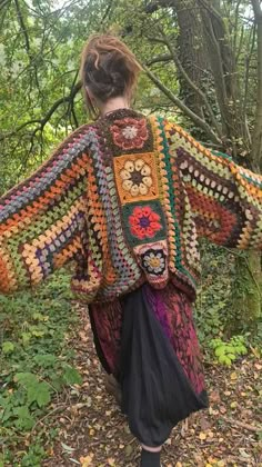 a woman is walking through the woods wearing a crocheted shawl with flowers on it