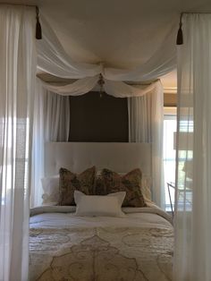 a bed with white drapes and pillows on it