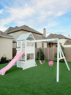 a white house with a pink slide and swing set in the back yard on artificial grass