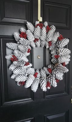 a wreath made out of pine cones hanging on the front door with red berries attached to it