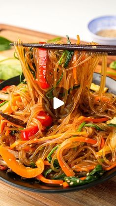 a plate full of noodles and vegetables with chopsticks sticking out of the top