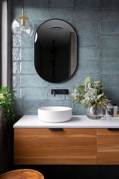 a bathroom sink with a round mirror above it next to a wooden cabinet and plant