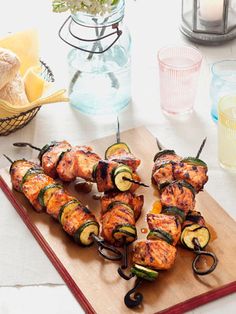 several skewered meats and vegetables on a cutting board next to some glasses