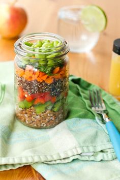 a mason jar filled with vegetables and seeds on top of a green napkin next to a fork