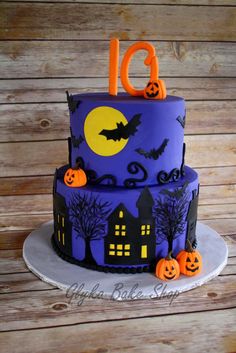 a three tiered cake decorated with purple icing and pumpkins on a wooden table