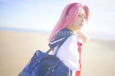 a young woman with pink hair carrying a blue bag on the beach in front of the ocean