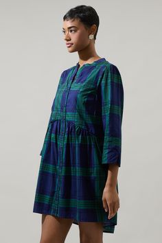 This statement-making, green and blue plaid dress features long sleeves followed by a button-down placket in the front. It has a flowy fit making it comfortable to move around. Style it with a simple bag for an effortlessly cute look.- Plaid- Pockets- Lined- Button down- Color: Navy GreenSize + Fit - Model is 5'10" and wearing size XS- Measurements taken from size S - Chest: 19"- Length: 33 3/4" Fabric Self: 100% Cotton, Lining: 100% Polyester Style Number STD14464P Blue And Green Plaid Dress, Plaid Mini Dresses With Button Closure, Blue Button-up Dress With Placket, Casual Button-up Plaid Dress, Green Plaid Dress, Blue Plaid Dress, Plaid Cotton Button-up Dress, Babydoll Style, Button Down Dress