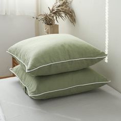 two green pillows sitting on top of a bed next to a plant in a vase