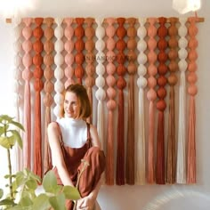 a woman sitting in front of a wall hanging with tassels