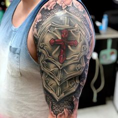 a man's arm with a cross and armor tattoo on it, while he is wearing a tank top