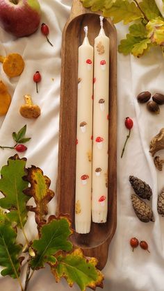 two white candles sitting on top of a wooden tray next to leaves and acorns