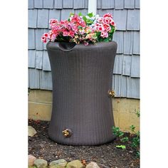 a brown wicker planter with pink flowers in it on the side of a house