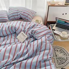 a bed covered in blue and red striped sheets with a laptop on top of it