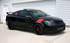 a black car with red stripes parked in front of a garage