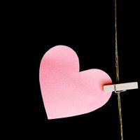 a pink paper heart hanging from a clothes peg on a black background with the string attached to it