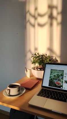 a laptop computer sitting on top of a wooden desk next to a cup of coffee