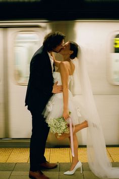 a bride and groom kissing on the subway platform