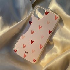 an iphone case with hearts on it laying on a white satin sheeted bed spread