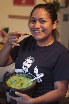 a woman is holding a bowl of food and eating it with a spoon in her hand