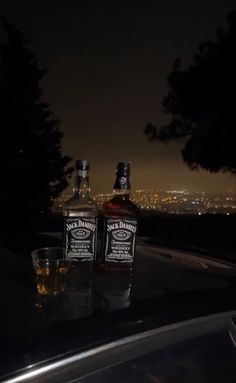 two bottles of whiskey sitting next to each other on top of a roof at night