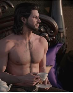 a shirtless man sitting on a bed holding a cup and saucer in front of him