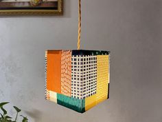 a multicolored square hanging from a string on a wall next to a potted plant