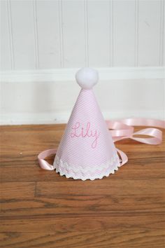 This adorable hat is beautifully crafted with a simply sweet pink stripe  It is our newest girl party hat addition!  A soft pink hand-stitched font adorns the front.  It is embellished with white ric rac trim soft pom pom on the tip of the hat.  This hat includes a ribbon and elastic attachment - cute and functional!  It really is cute and a must have for that memorable first birthday.   ** NOTE that this hat will be made exactly as the listing photo indicates.  It features a soft pink stripe fabric and a soft thin medium pink font.  It is a very delicate and beautiful hat and has quickly become our best seller!!  However, if you want a thicker font or a darker color for the wording, please contact us for a custom order. ** Our fabric hats are made for that wonderful first birthday party a Baby Birthday Hat, First Birthday Hat, Pink Girl Birthday, 1st Birthday Hats, First Birthday Hats, Party Supply Store, Hat Handmade, Birthday Crown, Pink Party