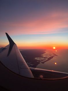 an airplane wing with the sun setting in the sky over water and land behind it