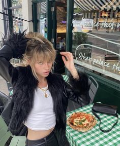 a woman standing in front of a table with a pizza on it and her hands behind her head