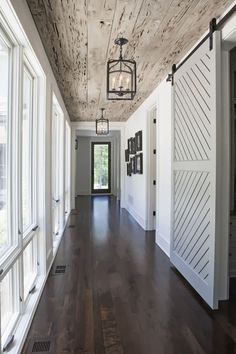 a long hallway with white walls and wood flooring is lit by an old fashioned light fixture