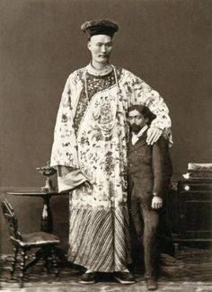 an old black and white photo of a man standing next to a woman in a dress