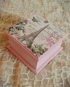 an open pink box with the eiffel tower on it's lid sitting on a lace tablecloth