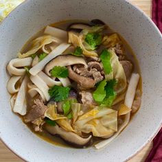 a white bowl filled with noodles and meats on top of a wooden cutting board