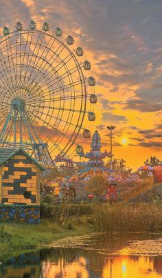 an amusement park with a ferris wheel and water pond in the foreground at sunset