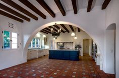 an arched kitchen with tile flooring and blue island in the center is surrounded by wood beams