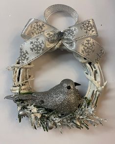 a silver bird sitting on top of a white wreath with snowflakes and bows